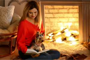 A dog lying on a woman's lap near a fireplace as background.
