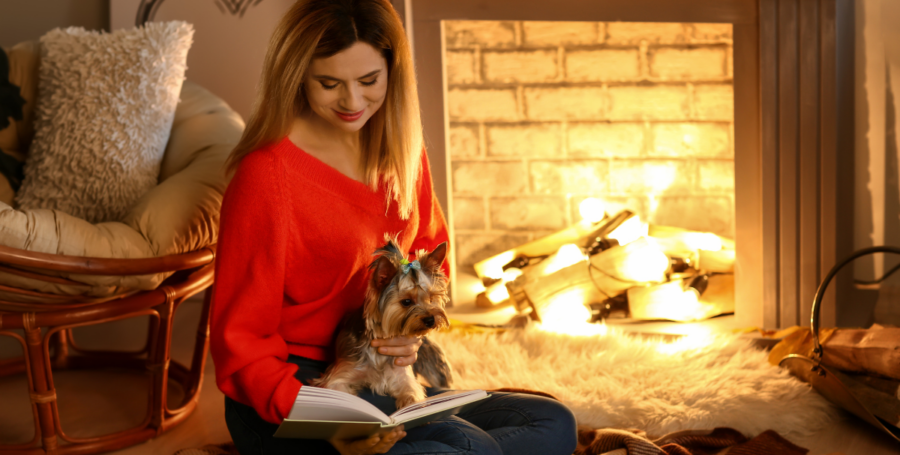 A dog lying on a woman's lap near a fireplace as background.